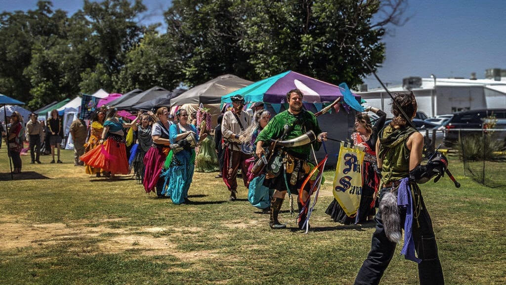 Guests and performers in colorful Renaissance-inspired costumes walking through the first West Texas Renaissance Festival in Odessa, Texas.